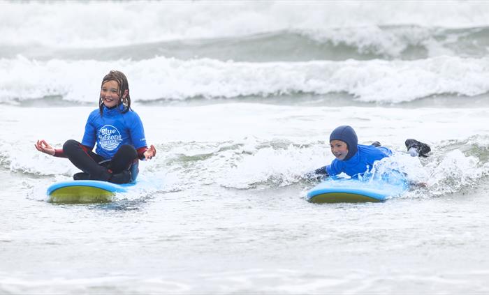 Children learning to surf with Blue Horizons on a Pembrokeshire beach, smiling in small waves